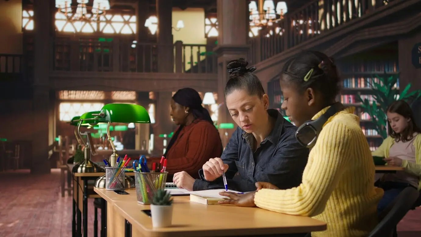 Weiße Nachhilfelehrkraft, die ein Grundschulmädchen an einem Tisch in der Bibliothek anleitet